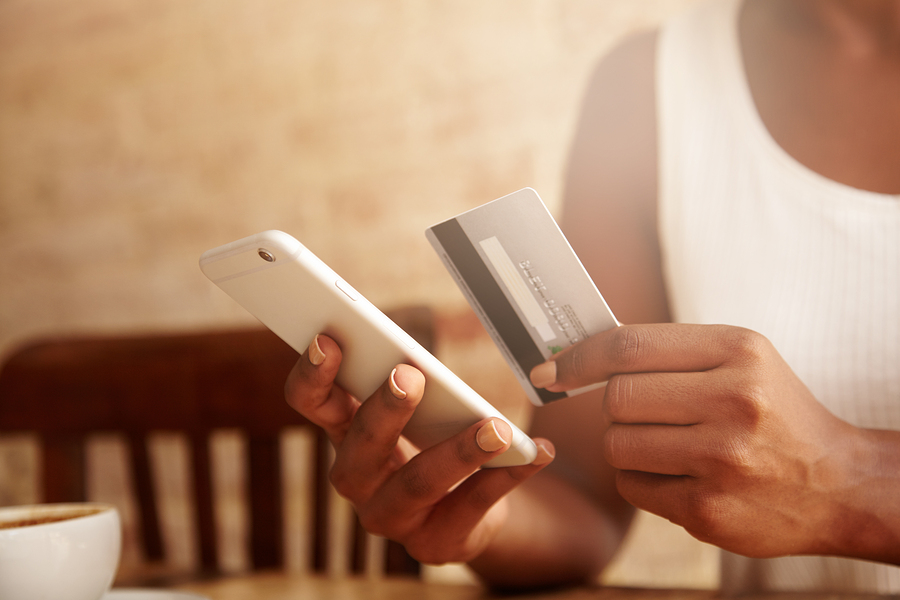 Cropped portrait of African American housewife wearing casual top using mobile phone entering information on her credit card while signing up on food delivery website while spending evening at home